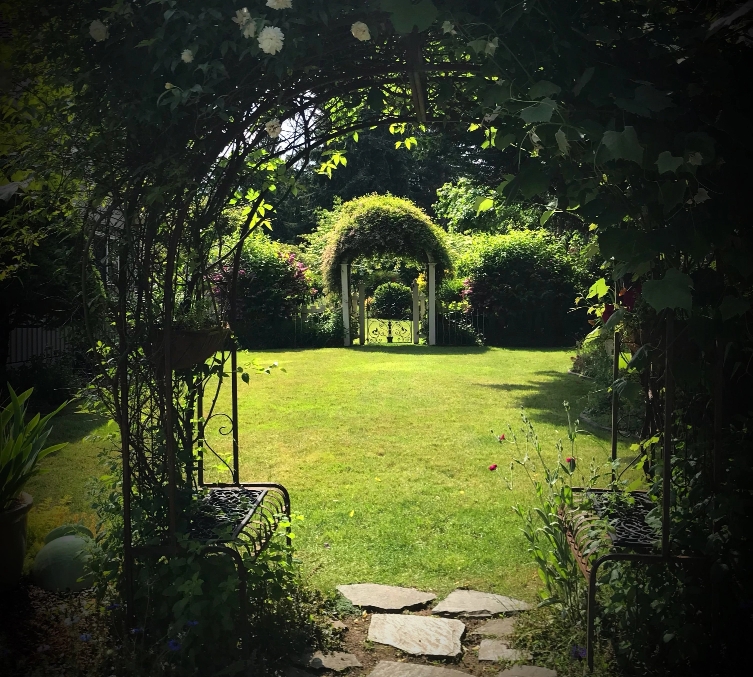 Jardin avec arbustes et arches végétales.